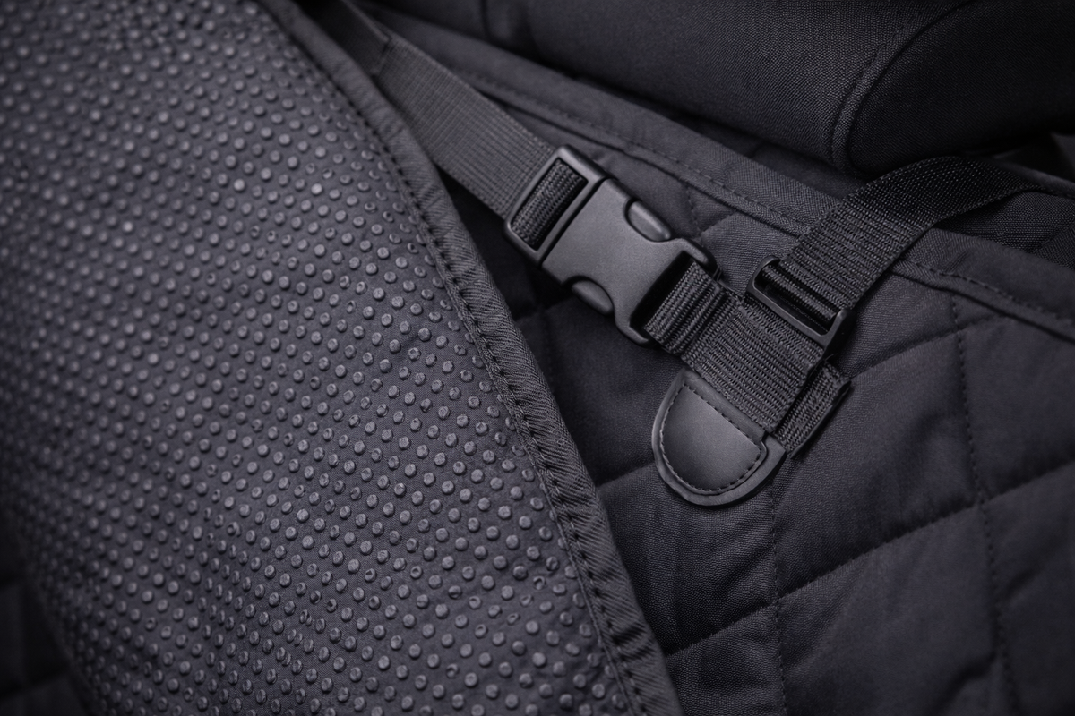 Close-up van antislip noppen aan de onderkant van een zwarte autodeken, met een riem en klikgesp die de deken vastzetten